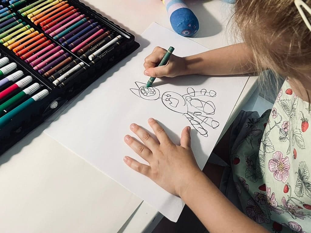Dziecko rysuje flamastrem przy otwartym zestawie kredek